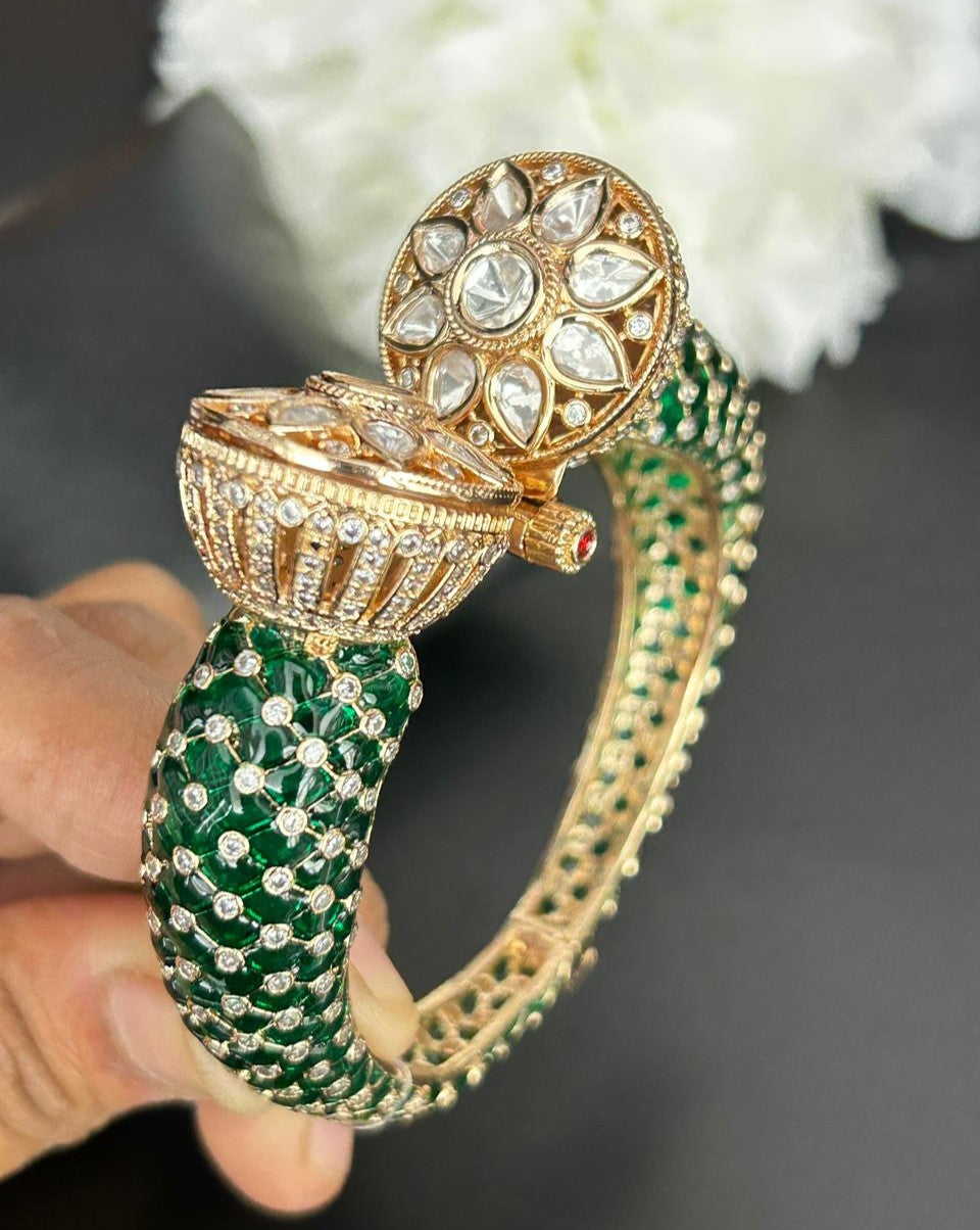 Gold and green bracelet with gemstones held by a hand against a blurred white flower background