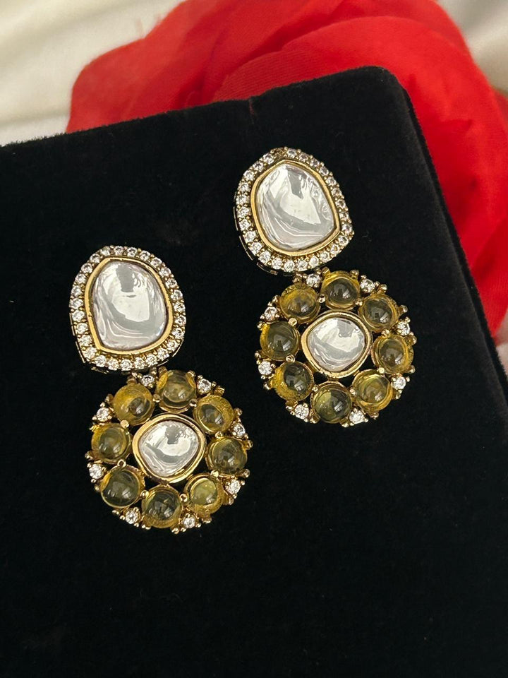 Gold and green gemstone earrings on a black stand with red fabric in the background