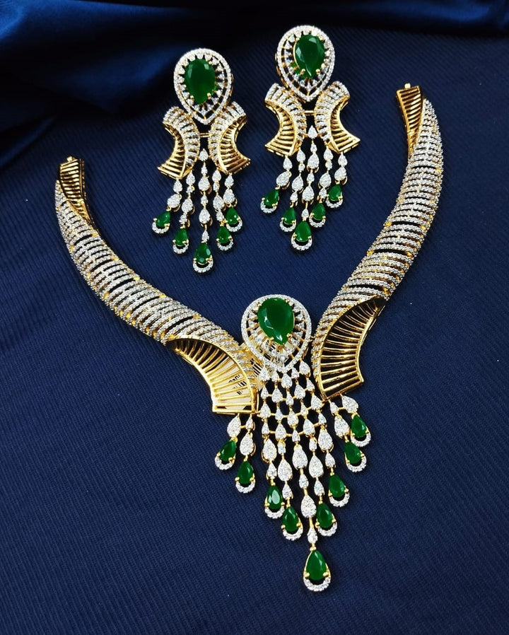 Gold and green gemstone necklace and earrings on a dark blue fabric background