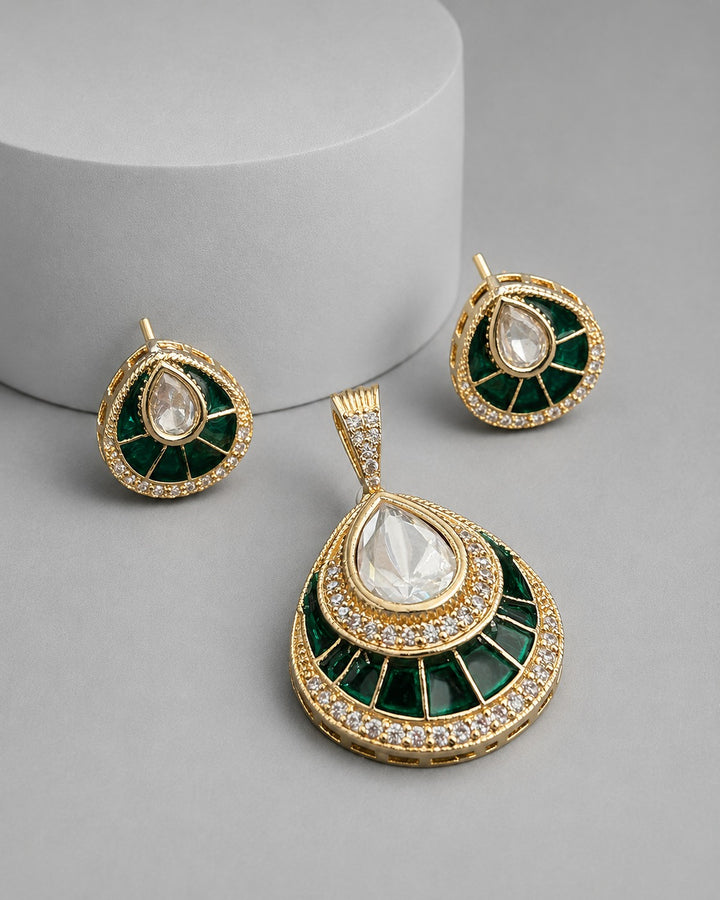 Gold and green teardrop pendant necklace with matching stud earrings, featuring a clear teardrop gemstone in the center of each piece and small clear stones around the borders, displayed on a gray background with a white cylindrical prop.