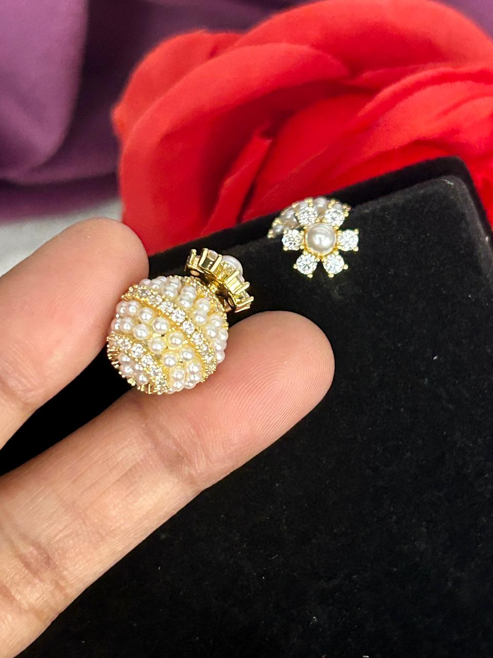 Gold and pearl earrings held by a hand with a red flower in the background.