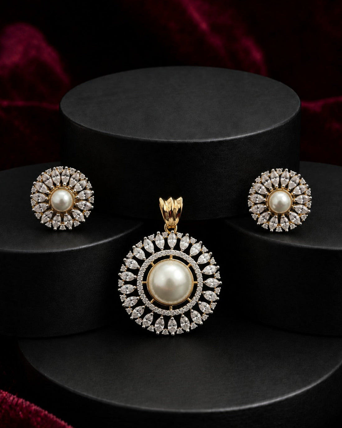 Gold and pearl jewelry set featuring a round pendant and matching stud earrings, displayed on black cylindrical pedestals against a dark red velvet background.