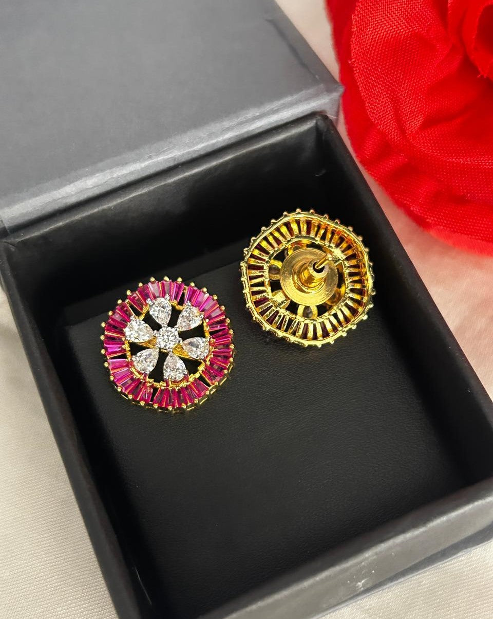 Gold and pink earrings in a black box with a red flower in the background