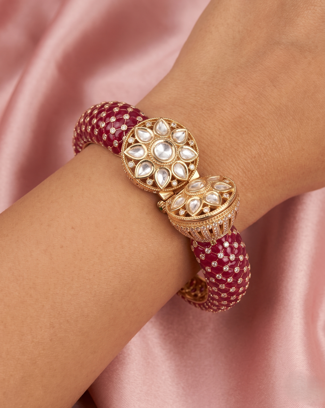 Gold and red bracelet on a wrist with a pink satin background