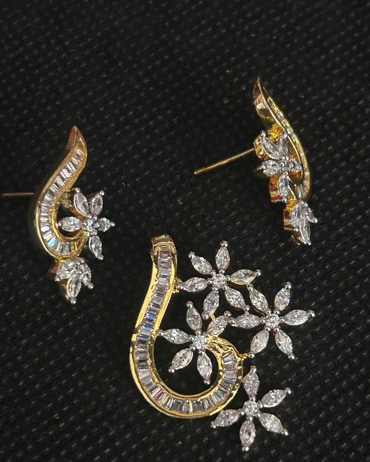 Gold and silver-tone stud earrings with floral and crescent motifs set with clear stones, displayed on a textured black background.