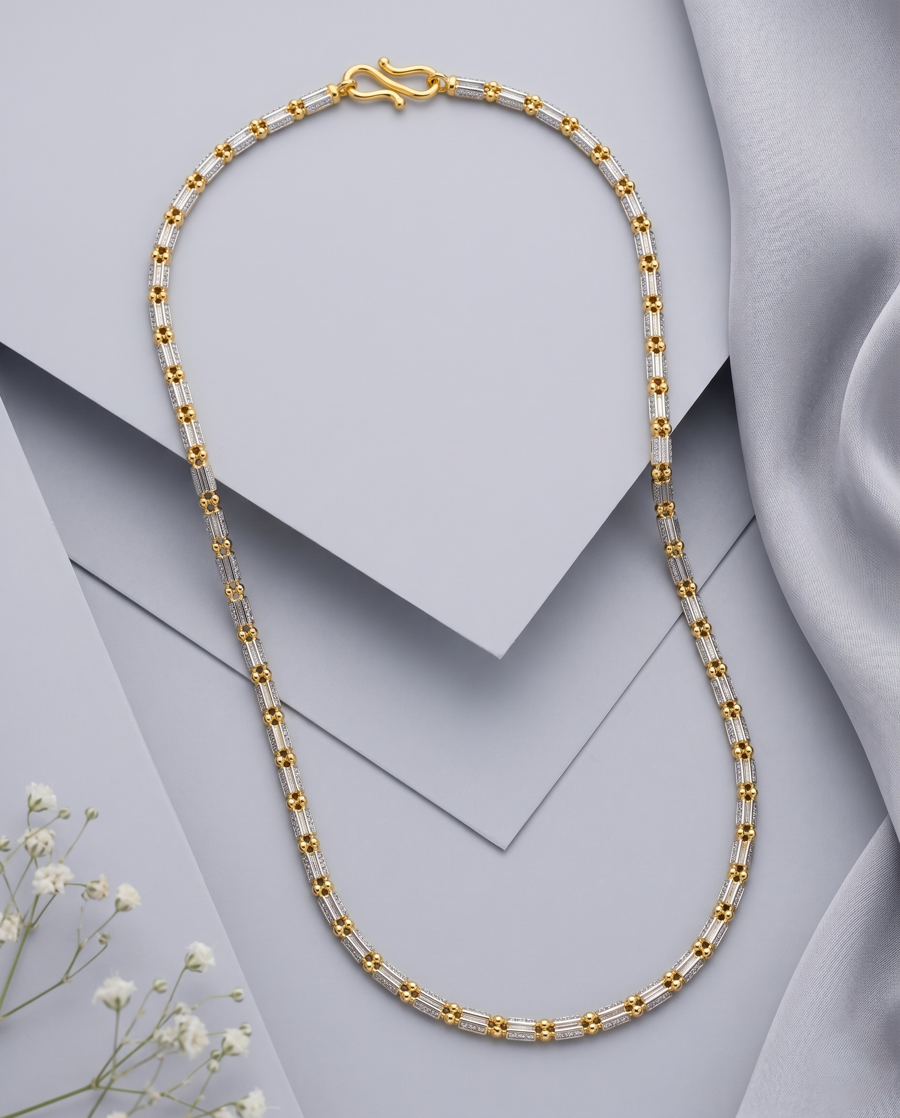 Gold and silver beaded necklace on a light gray background with white flowers.