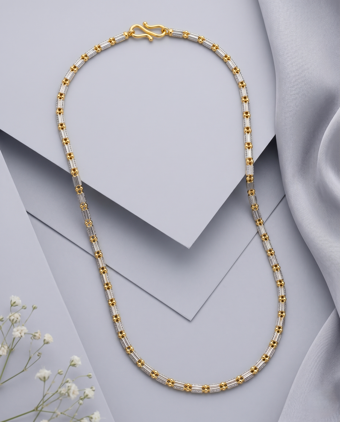 Gold and silver beaded necklace on a light gray background with white flowers.