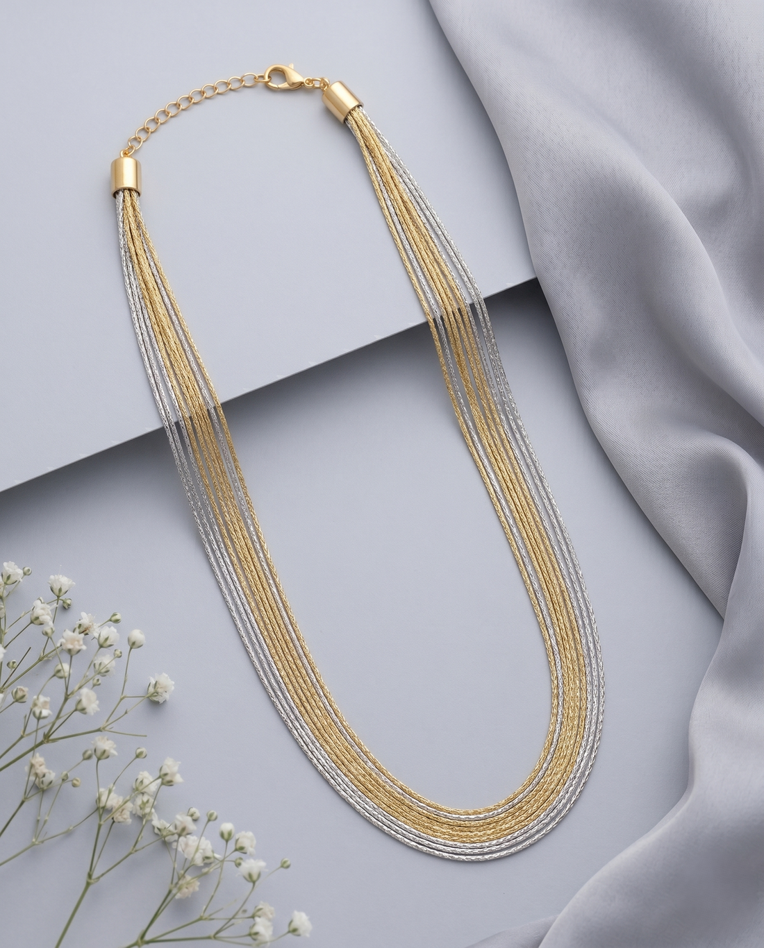 Gold and silver multi-strand necklace on a light gray background with a soft fabric texture.