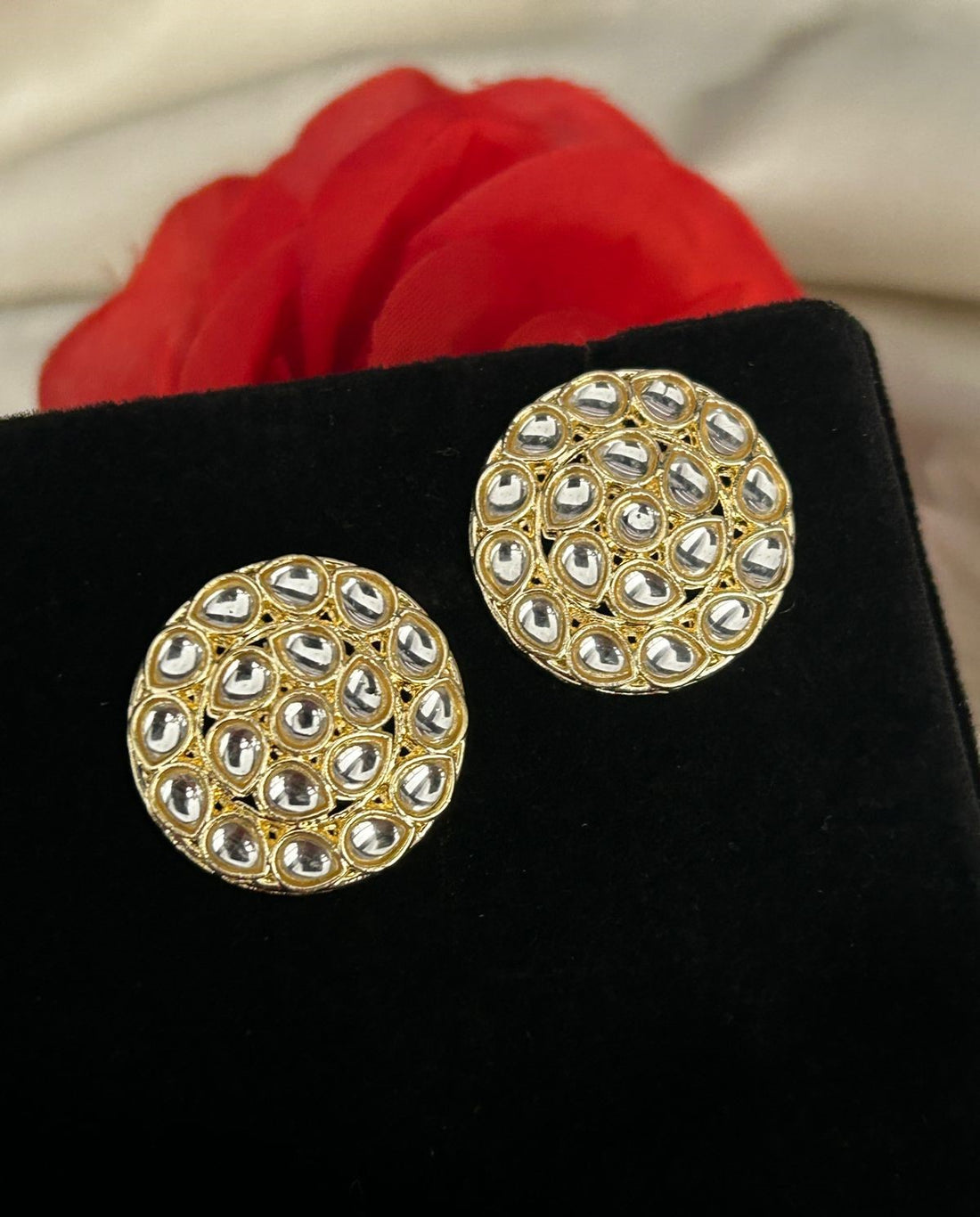 Gold and silver round earrings on a black surface with a red flower in the background