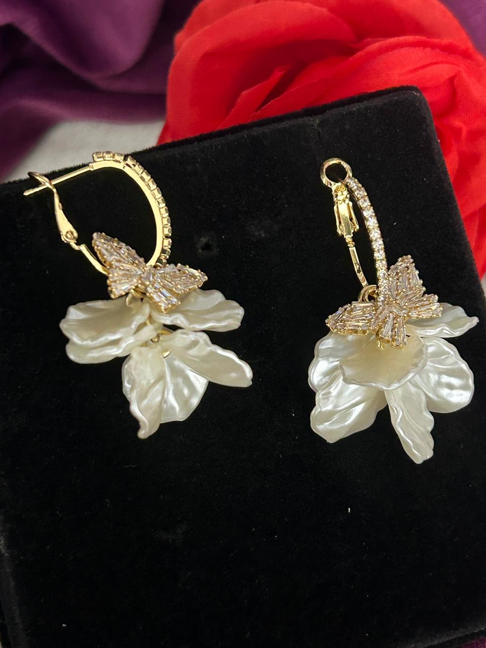 Gold and white floral earrings on a black background
