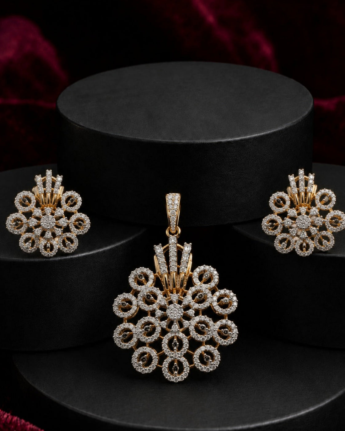 Gold and white stone jewelry set featuring a pendant, matching earrings, and a small box, displayed on black cylindrical pedestals against a dark red velvet background.