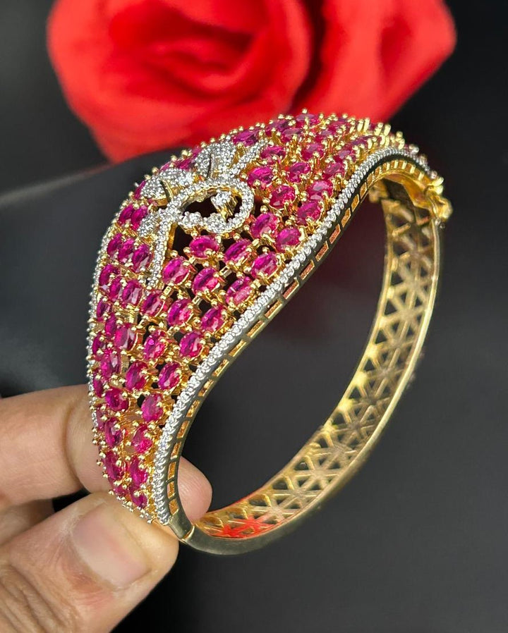 Gold bangle with pink stones held by a hand against a dark background