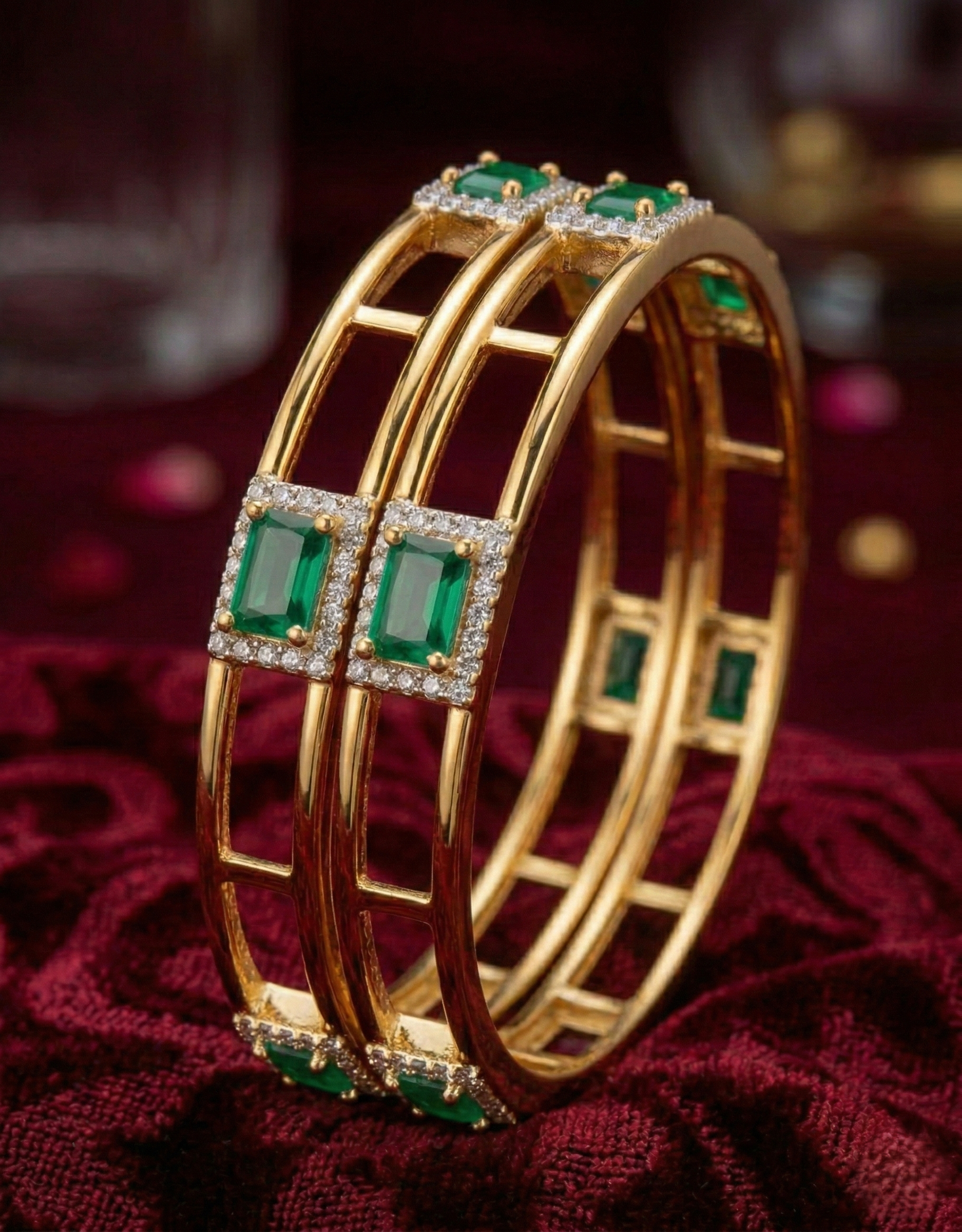 Gold bangles with emerald and diamond accents on a red fabric background