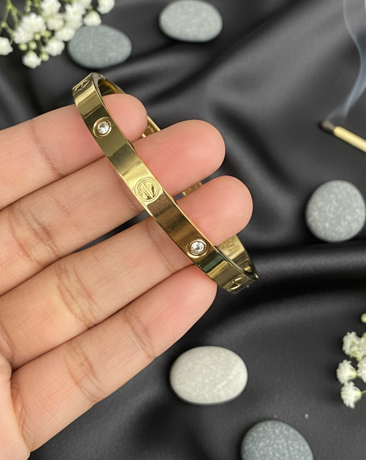 Gold bracelet held in a hand with a dark fabric background