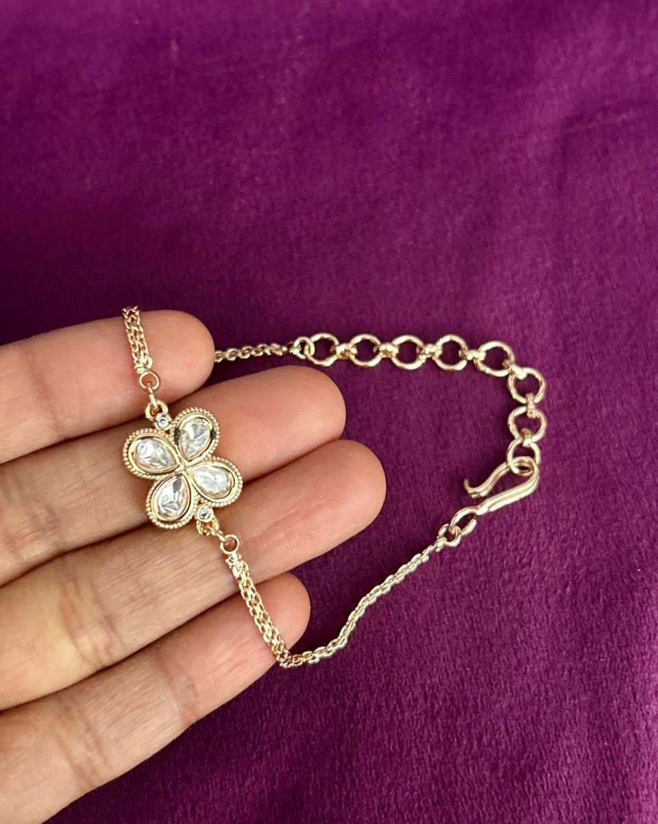 Gold bracelet with a clover-shaped charm held by a hand against a purple background
