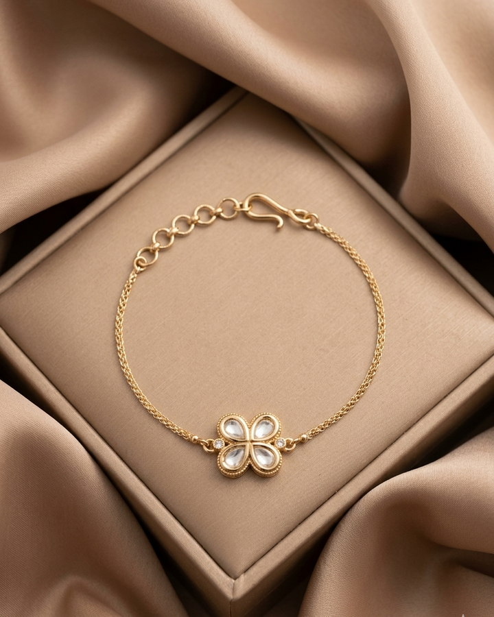 Gold bracelet with a clover-shaped clasp on a beige fabric background