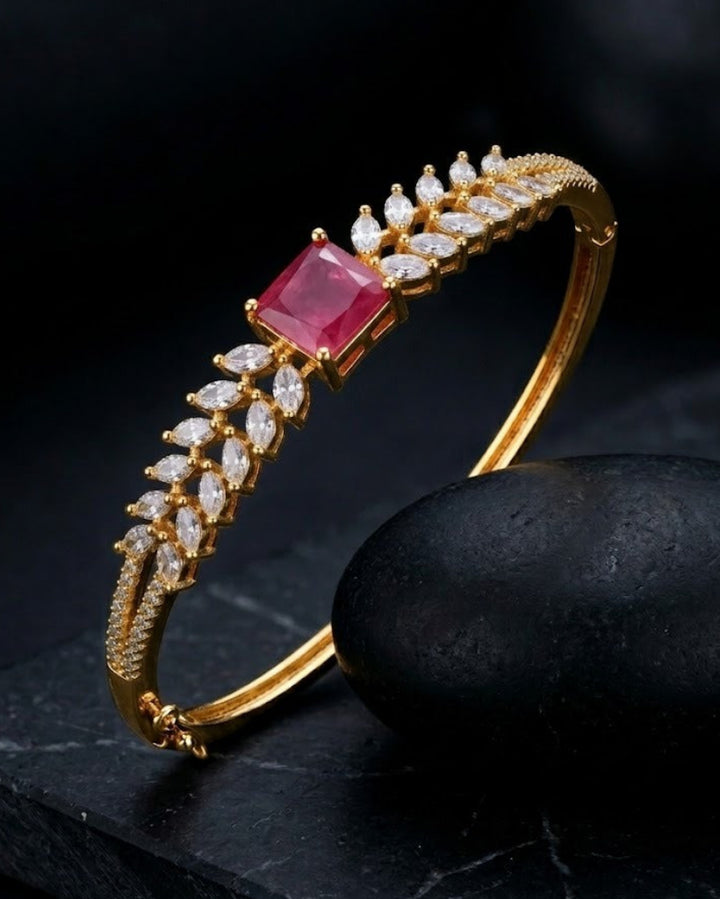 Gold bracelet with a red gemstone and diamond accents on a dark surface