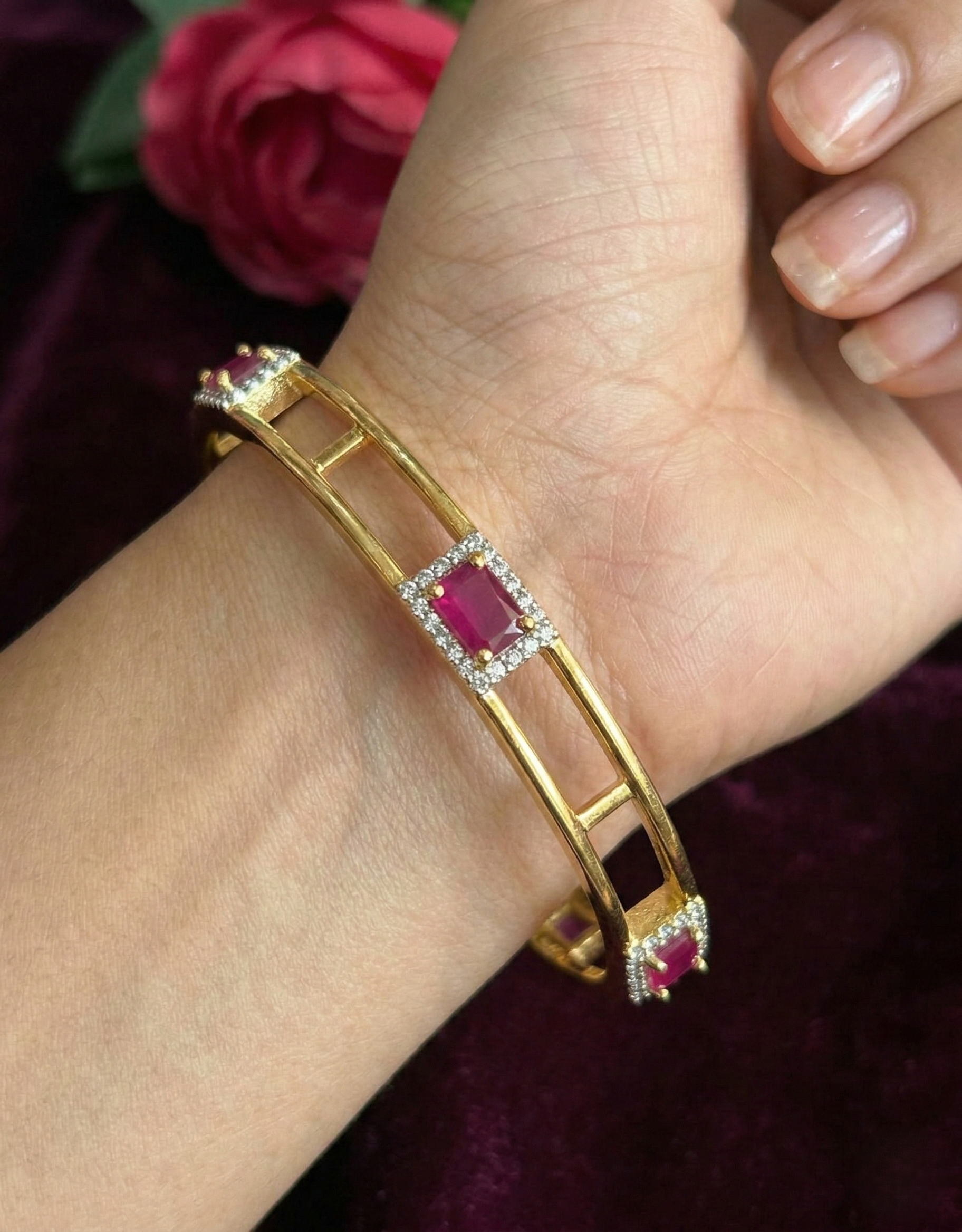 Gold bracelet with a red gemstone worn on a wrist, against a dark background.