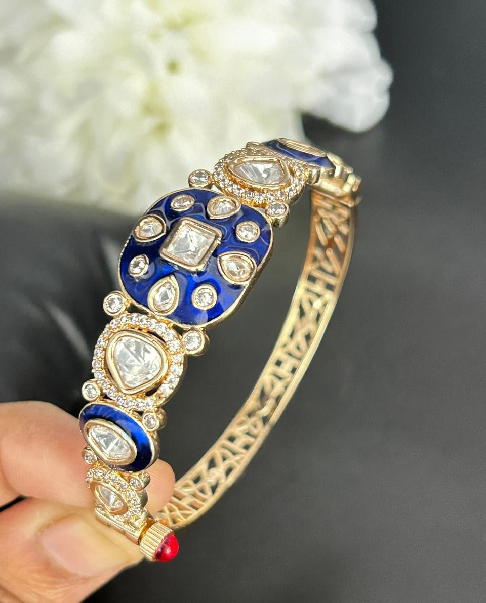Gold bracelet with blue and white gemstones held by a hand against a blurred background
