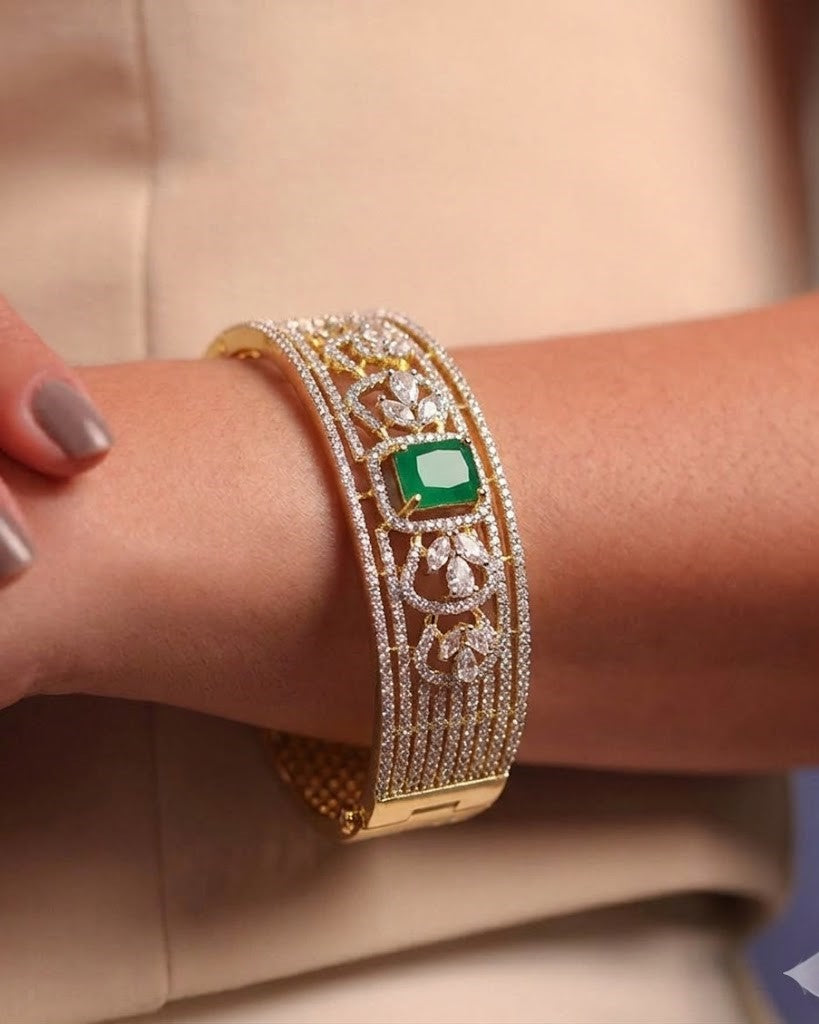 Gold bracelet with emerald stone on a wrist against a beige background
