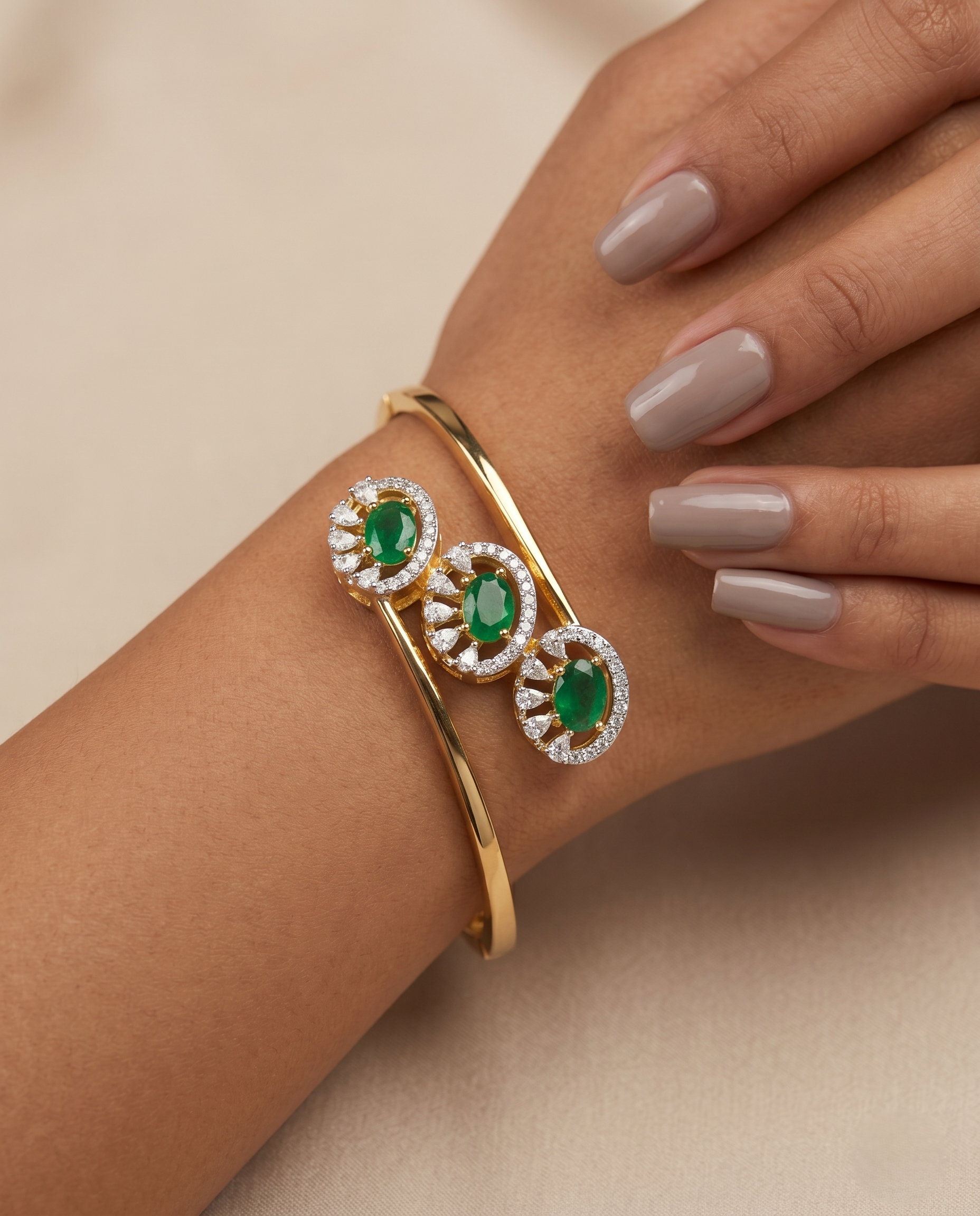 Gold bracelet with emerald stones on a hand against a beige background