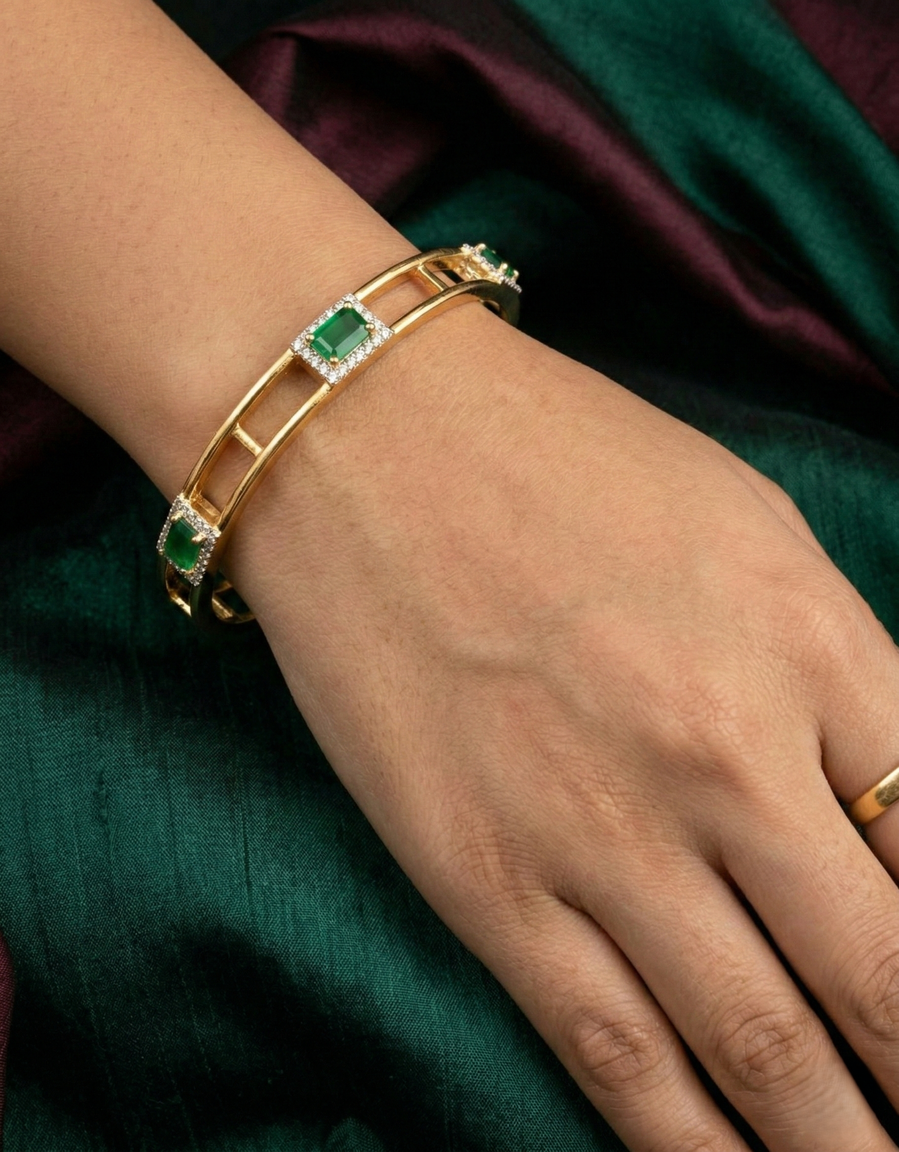 Gold bracelet with emerald stones on a wrist against a green fabric background