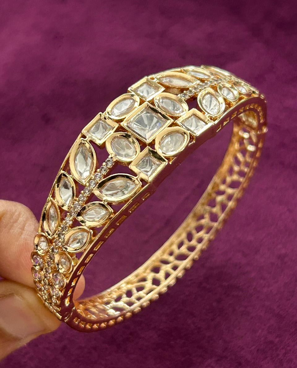 Gold bracelet with gemstones held against a purple background