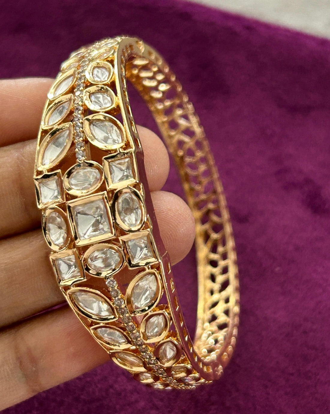 Gold bracelet with gemstones held by a hand on a purple fabric background