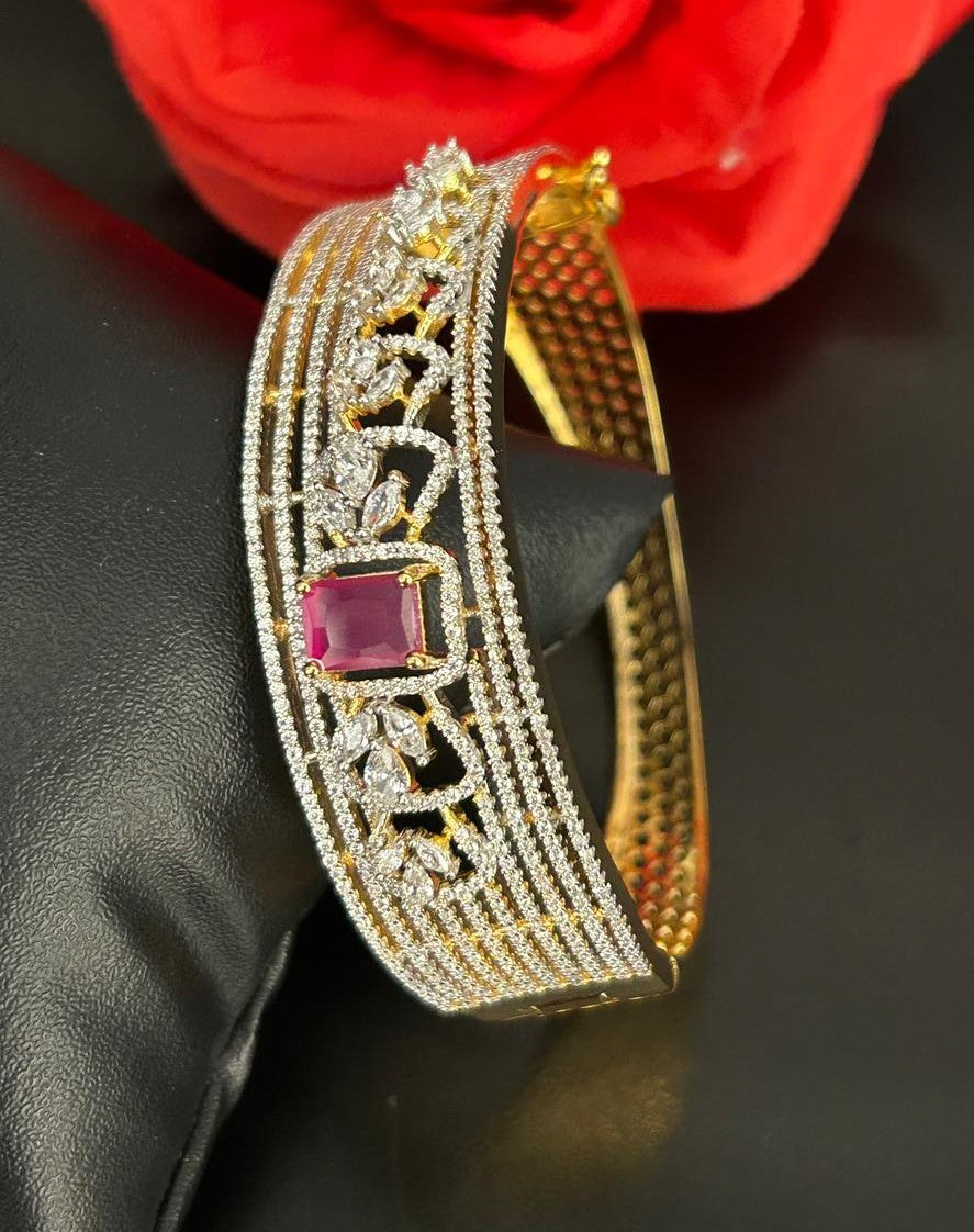 Gold bracelet with gemstones on a dark surface with a red flower in the background