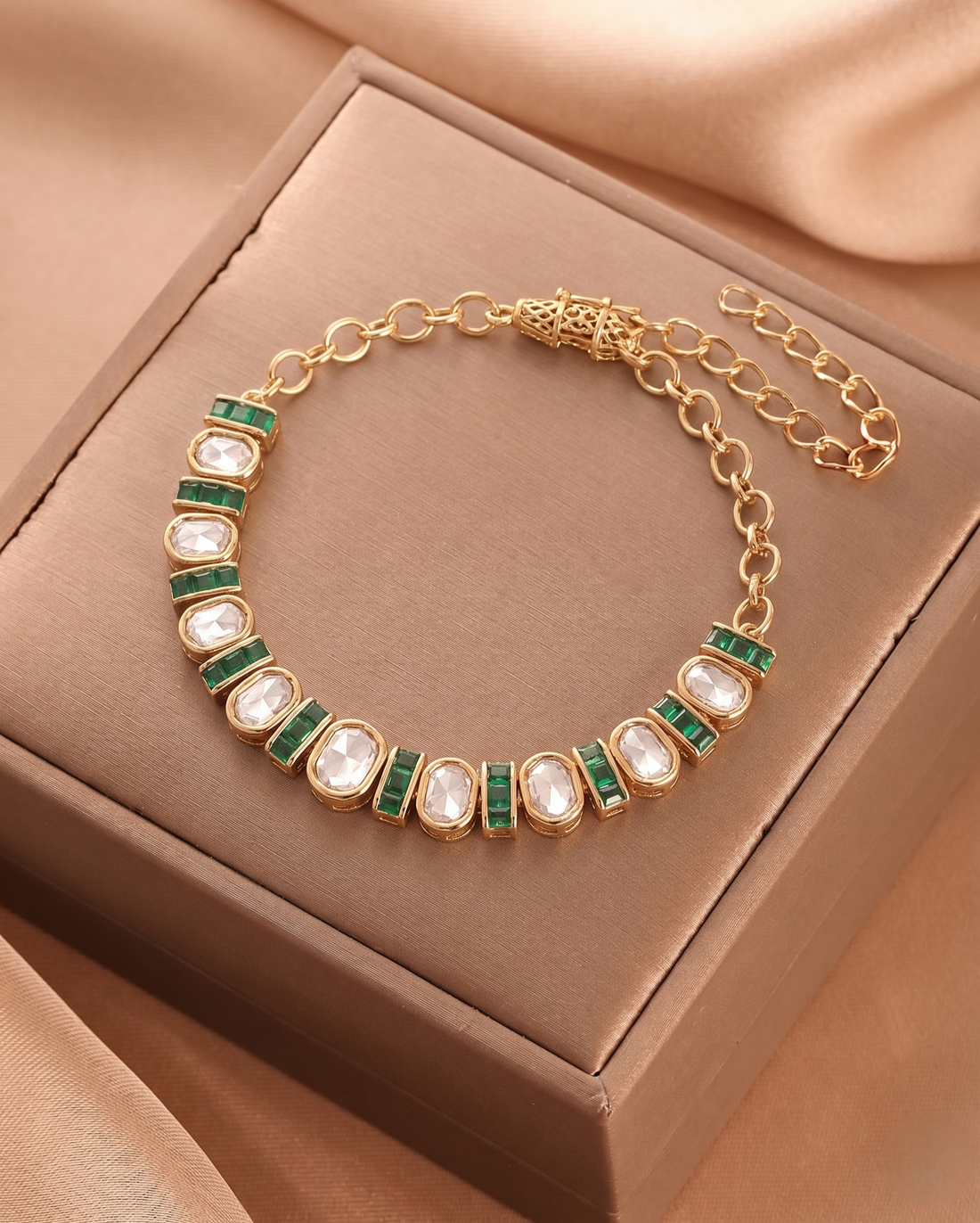 Gold bracelet with green and white stones on a brown box