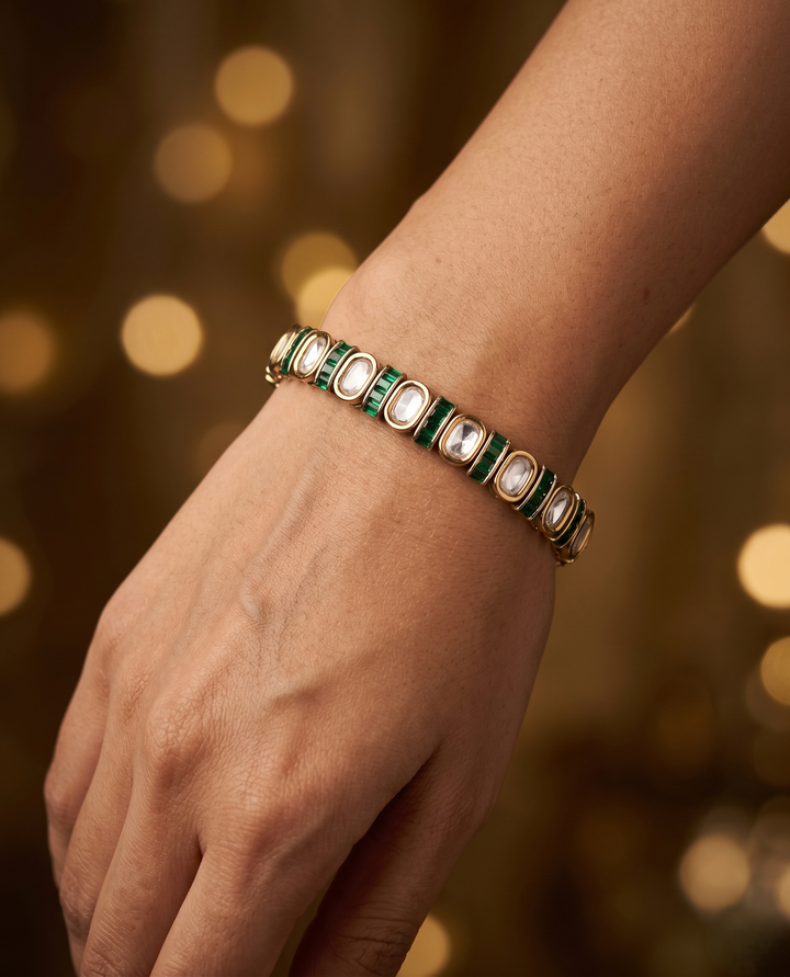 Gold bracelet with green and white stones on a wrist against a blurred warm background