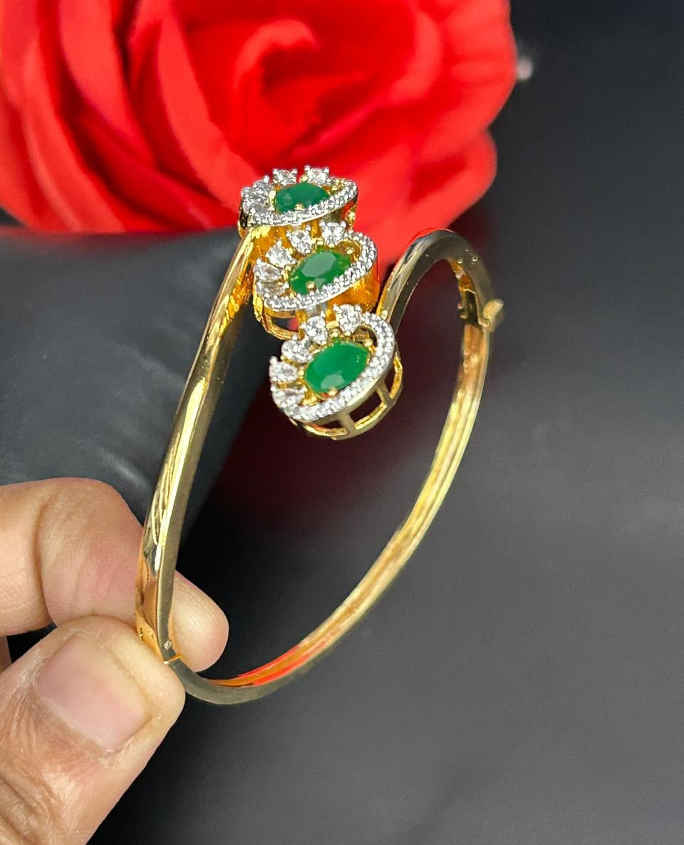 Gold bracelet with green gemstones held by a hand against a red rose background