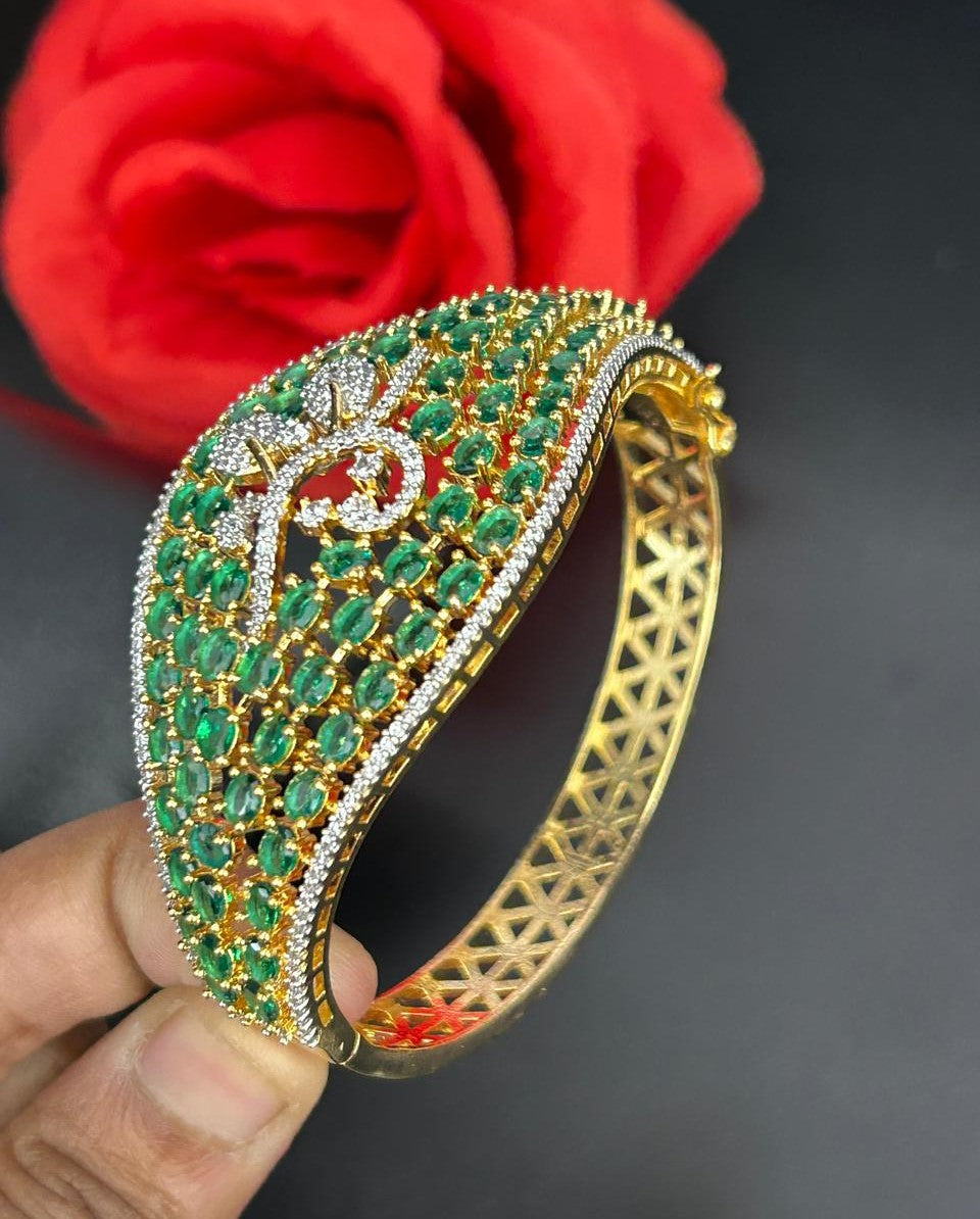 Gold bracelet with green gemstones held by a hand against a red rose on a dark background