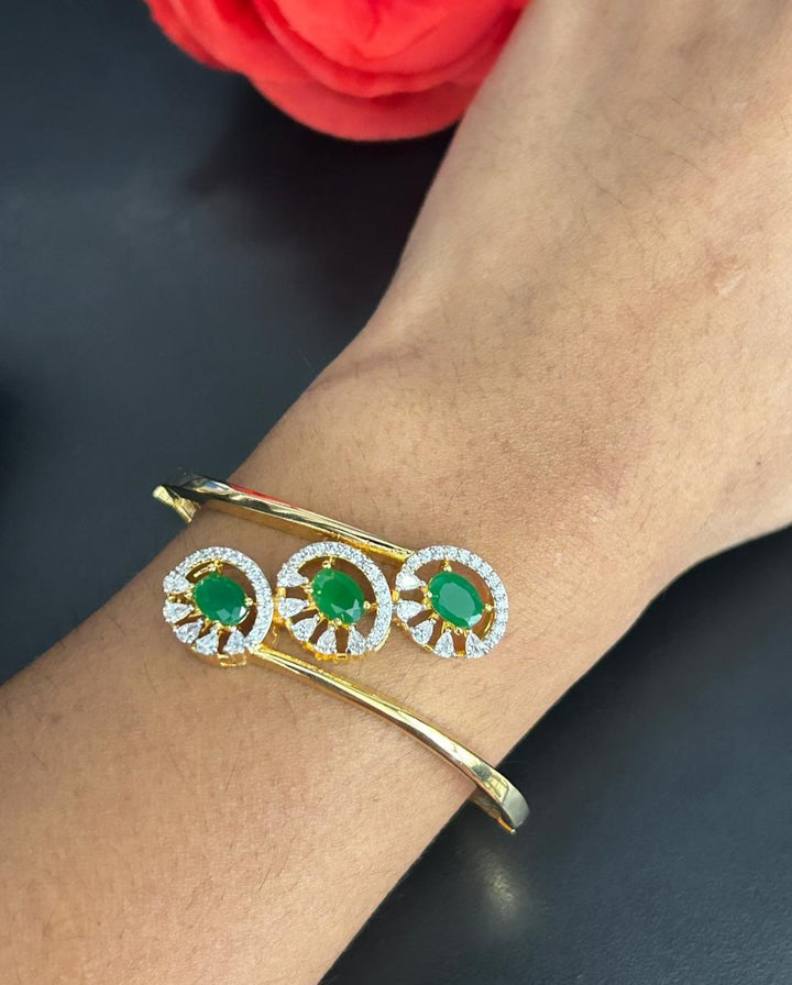 Gold bracelet with green gemstones on a wrist against a dark background
