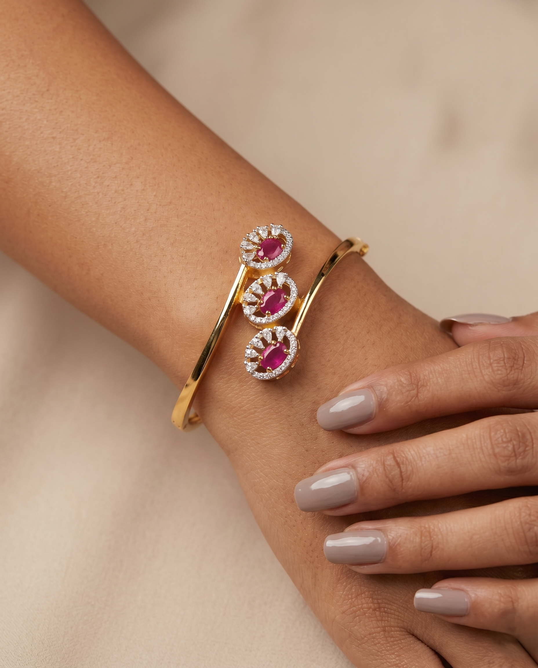 Gold bracelet with pink gemstones on a wrist against a beige background