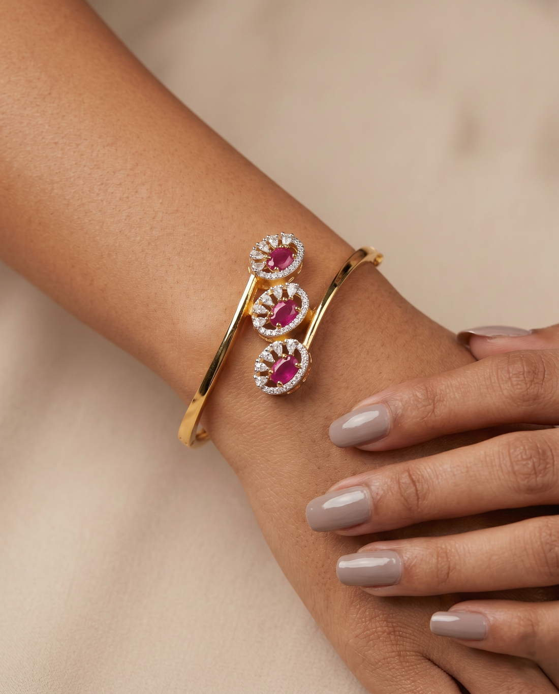 Gold bracelet with pink gemstones on a wrist against a beige background