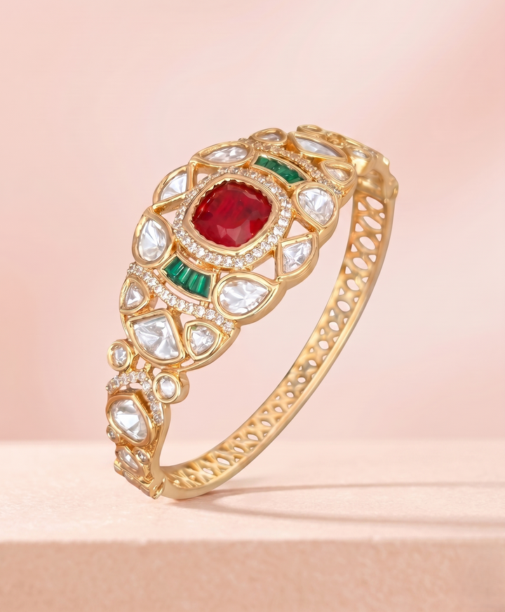 Gold bracelet with red and green gemstones on a pink background