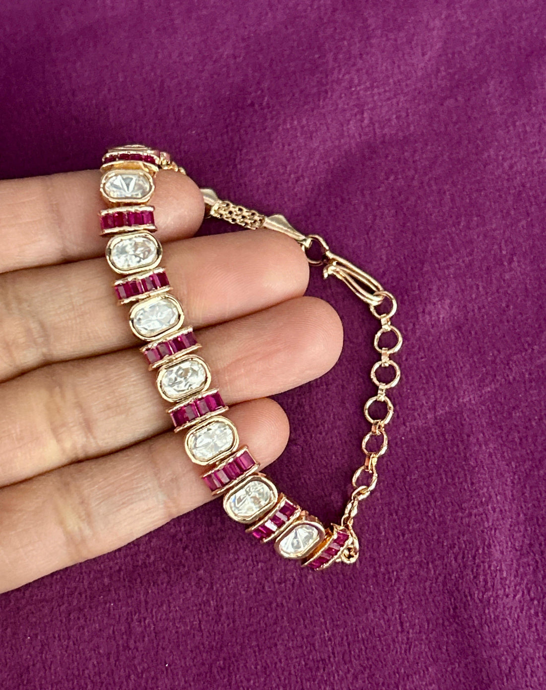 Gold bracelet with red and white stones held by a hand on a purple background