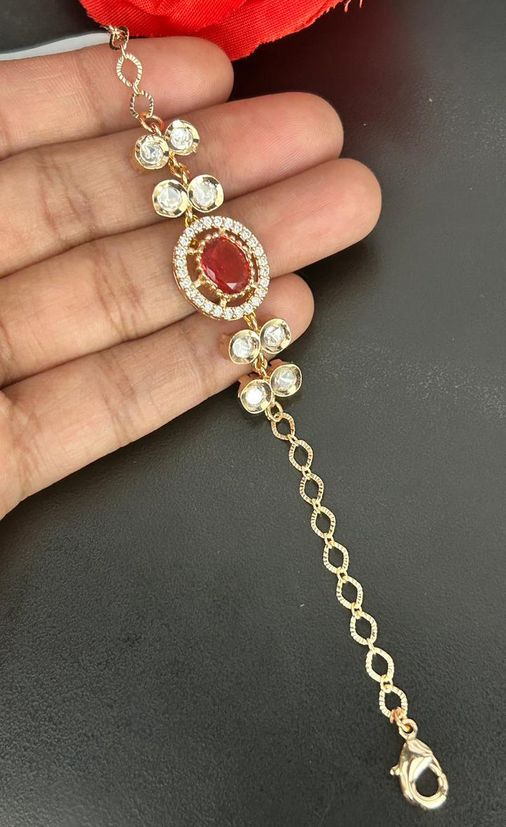 Gold bracelet with red gemstone held by a hand on a dark background
