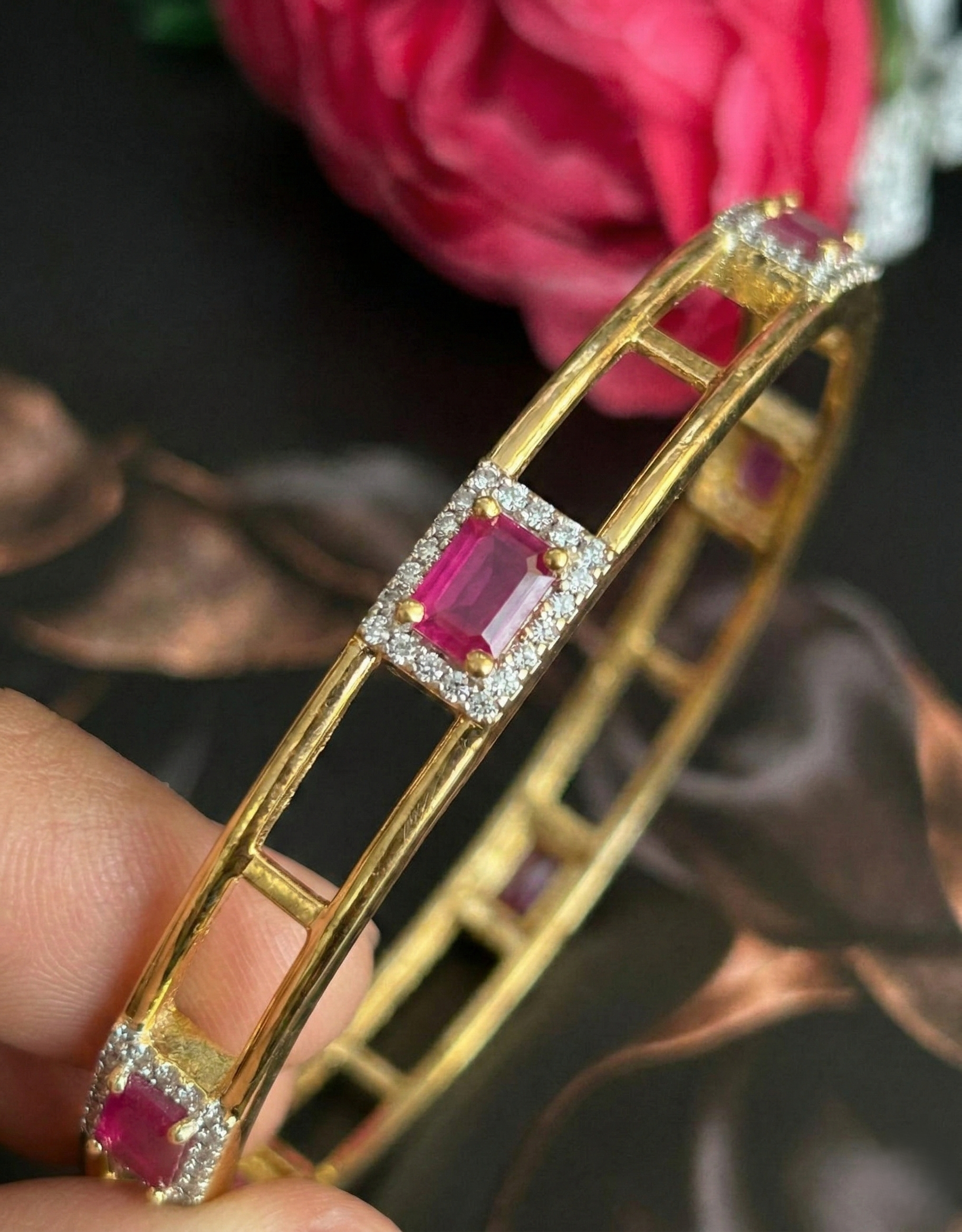 Gold bracelet with red gemstones held by a hand against a blurred floral background