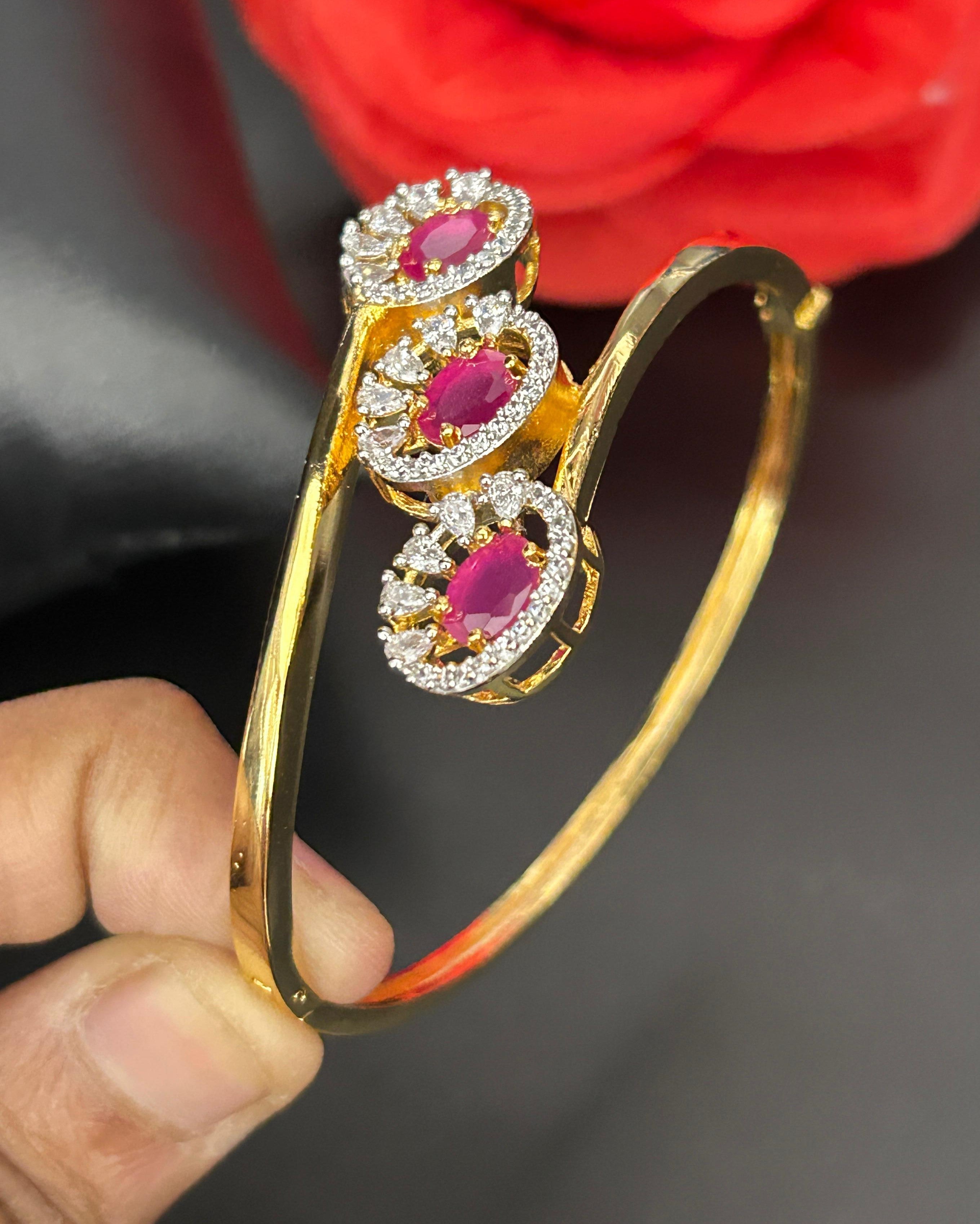 Gold bracelet with red gemstones held by a hand against a dark background