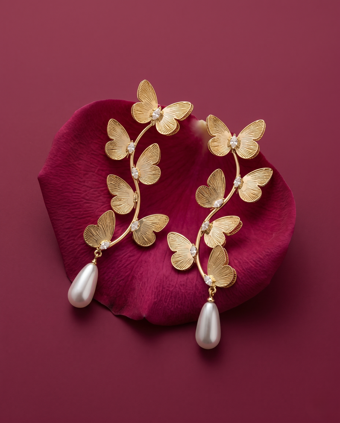 Gold butterfly earrings with pearl drops on a red petal background