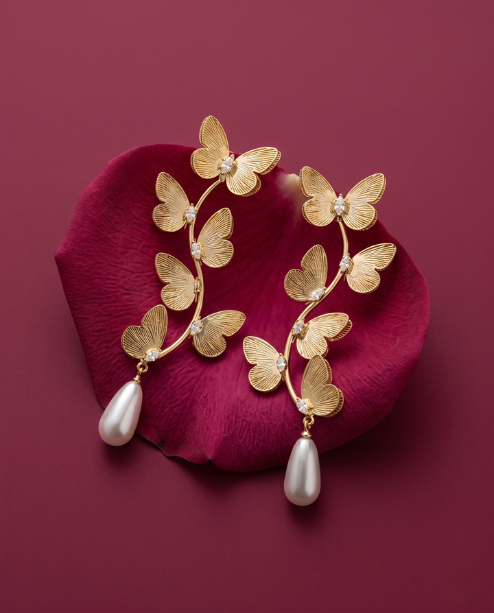 Gold butterfly earrings with pearl drops on a red petal background