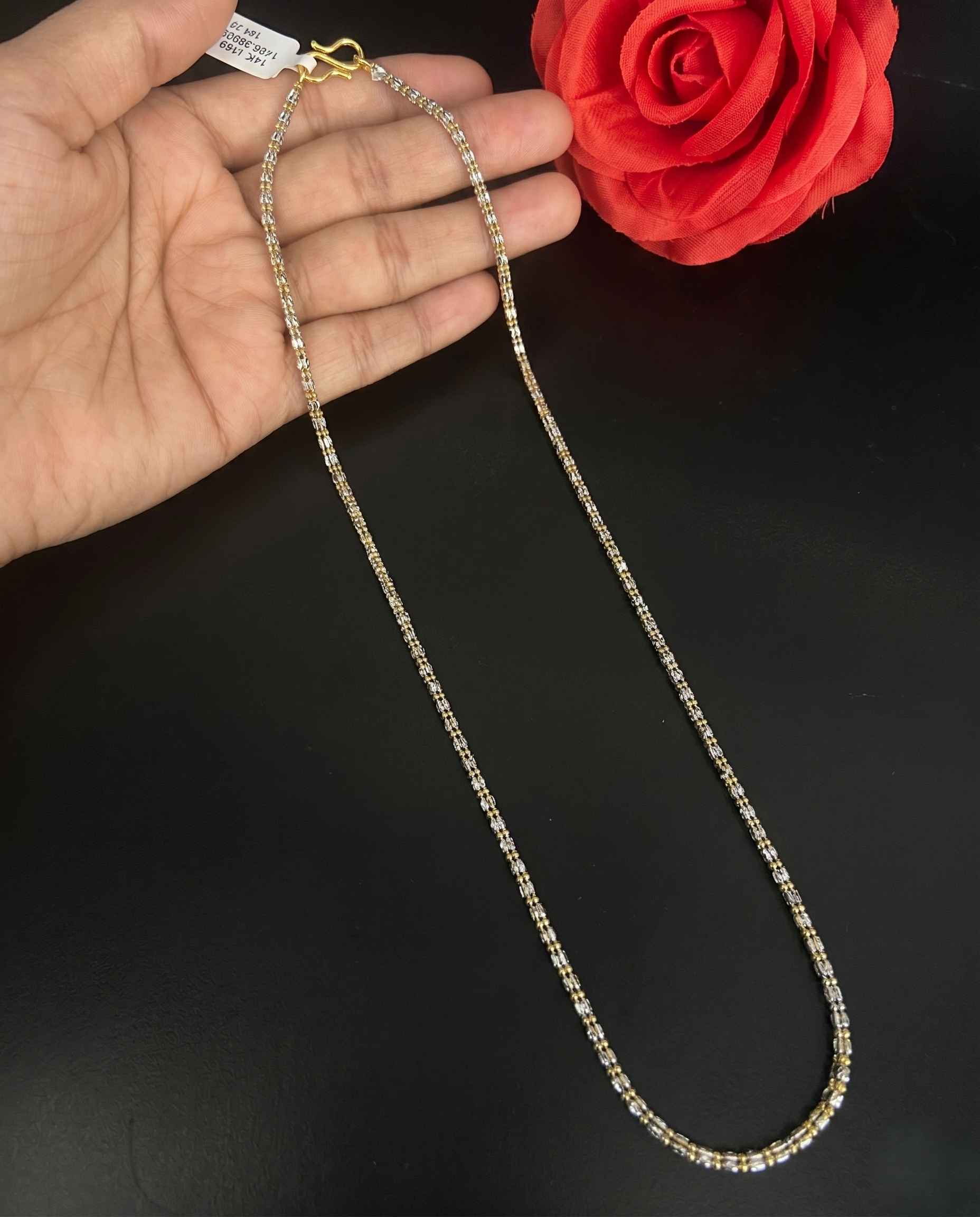 Gold chain held by a hand with a red rose in the background