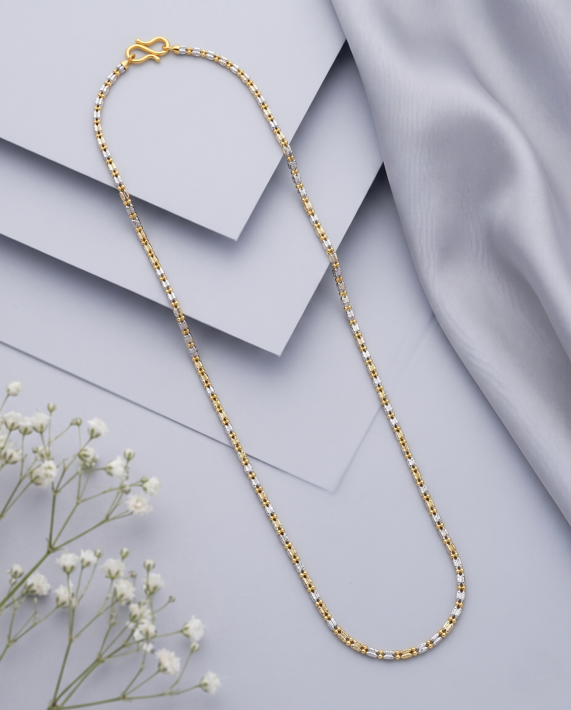 Gold chain necklace on a light gray fabric background with small white flowers.