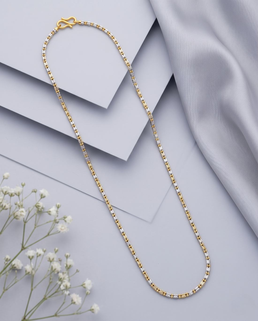 Gold chain necklace on a light gray fabric background with small white flowers.