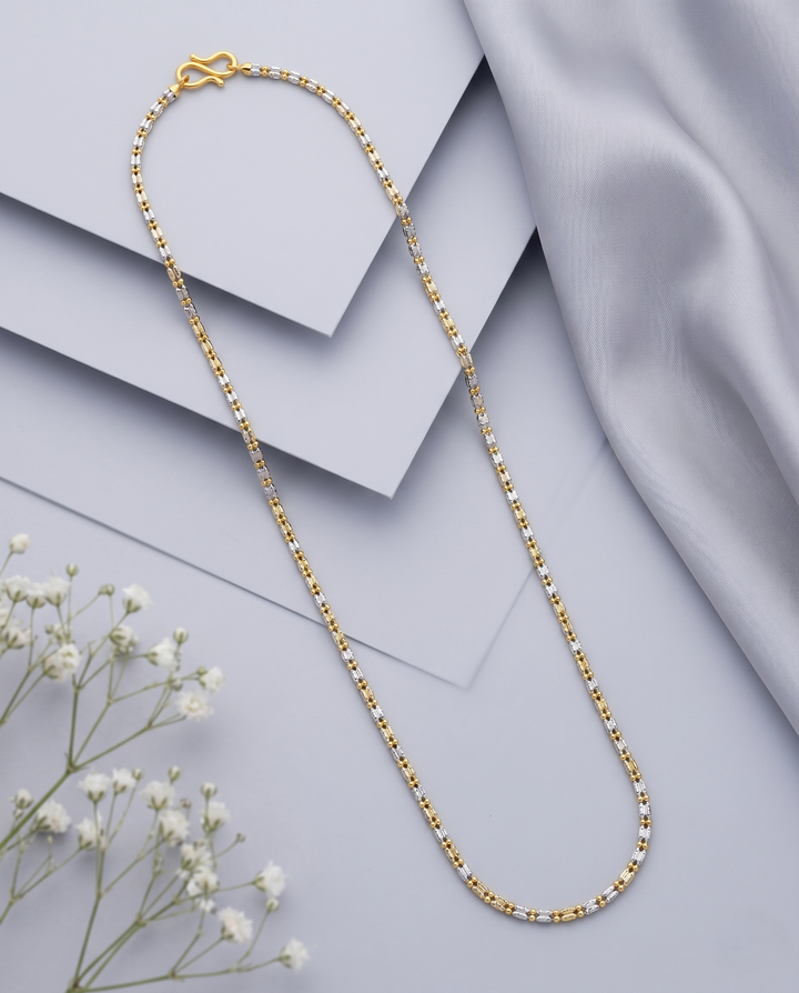 Gold chain necklace on a light gray fabric background with small white flowers.