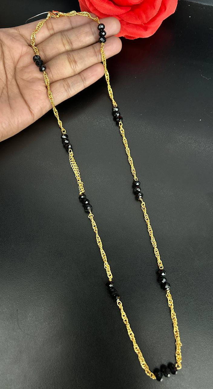 Gold chain with black beads held by a hand on a dark background