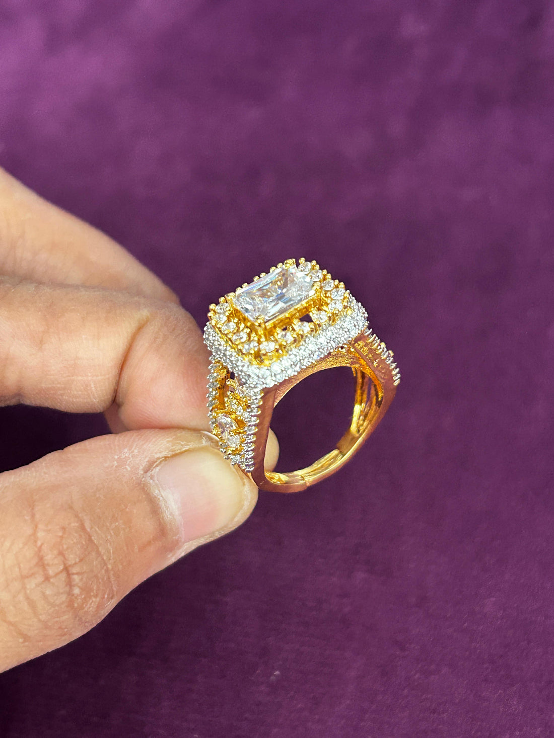 Gold and diamond ring held by a hand against a purple background