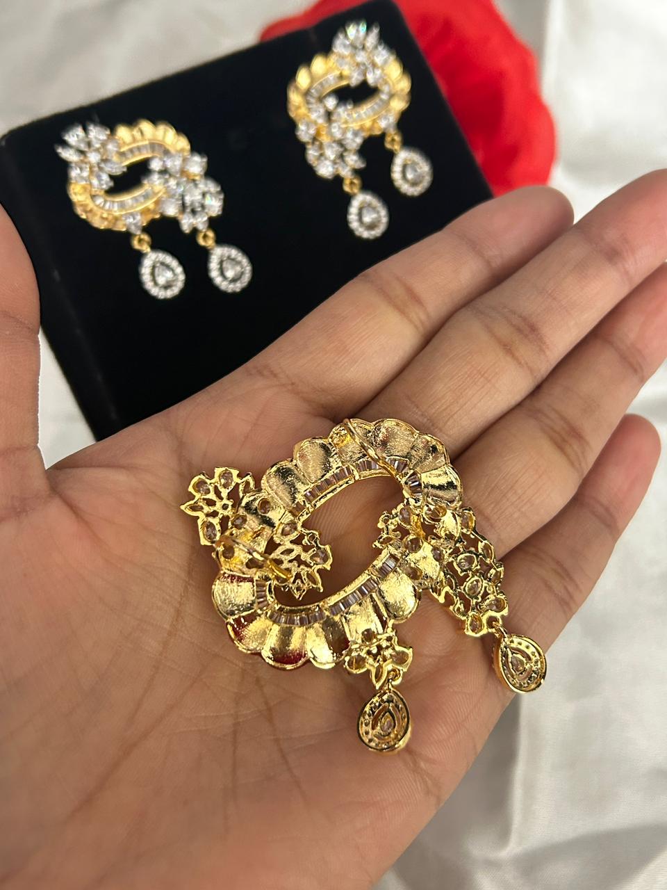 Gold earrings displayed on a hand with a black box in the background